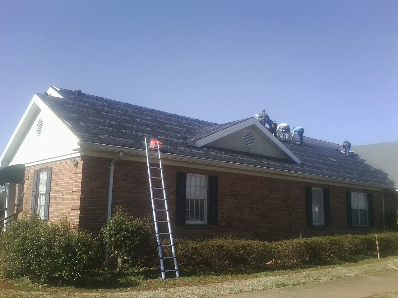 Crew tearing shingles off a brick ranch roof with a ladder set — Metal Roof Repair work by our crew in Stevenson Ranch