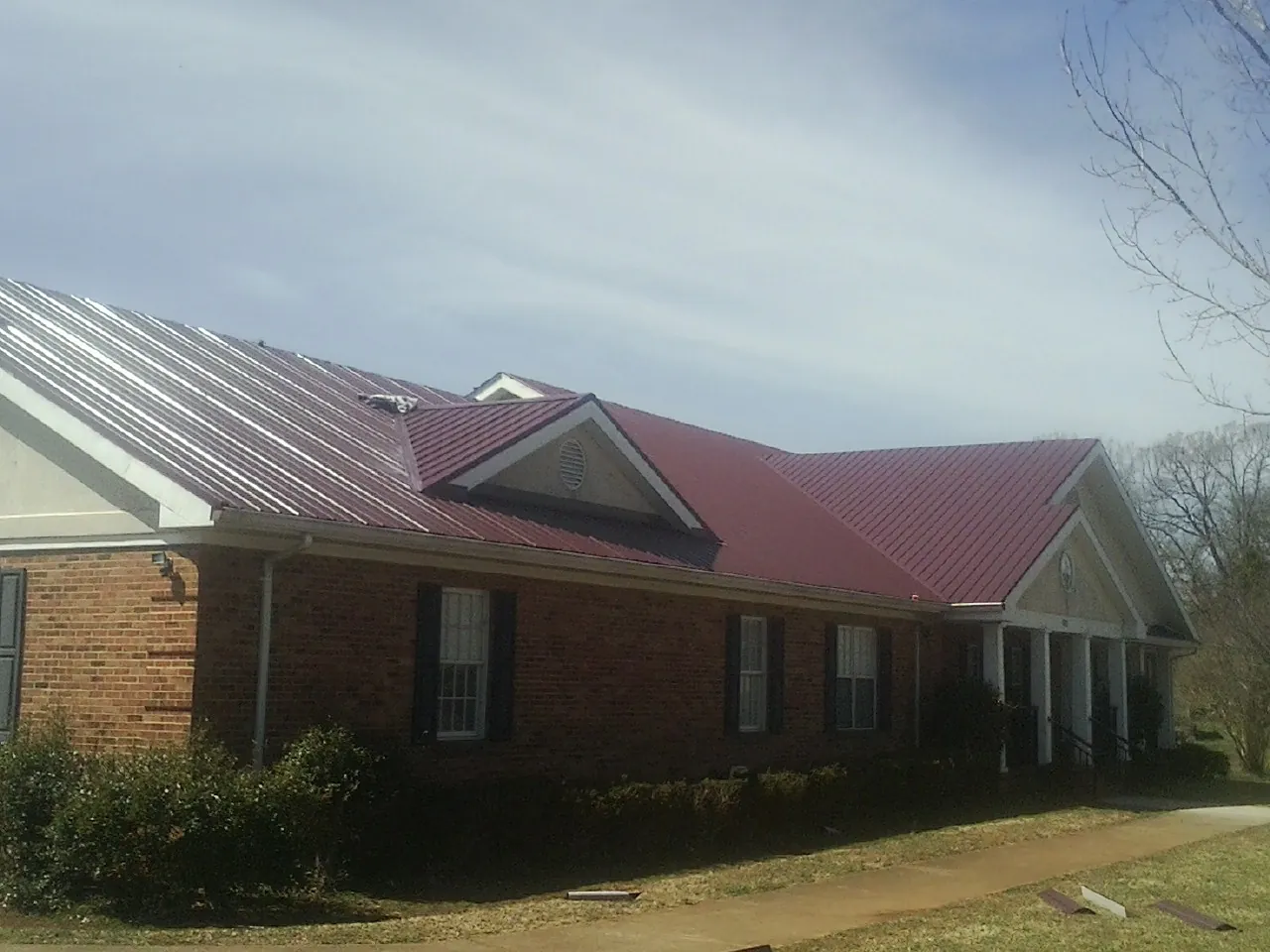 Red metal roof with gabled entries on a long brick building, from a Hail Damage Roof Repair job in Stevenson Ranch